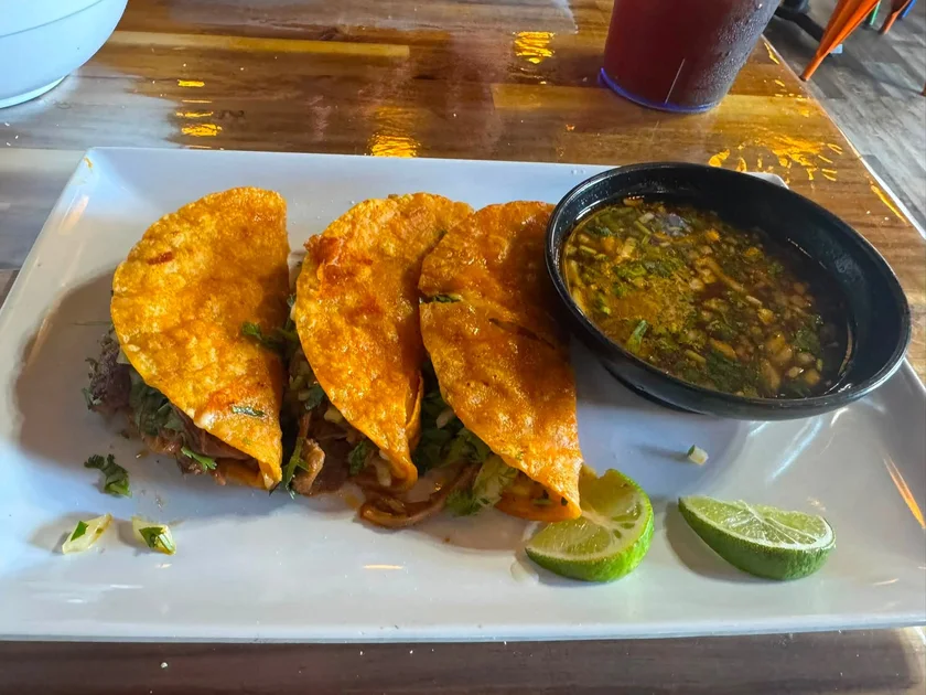 Three birria tacos with consommé and lime at Nina's Tacos