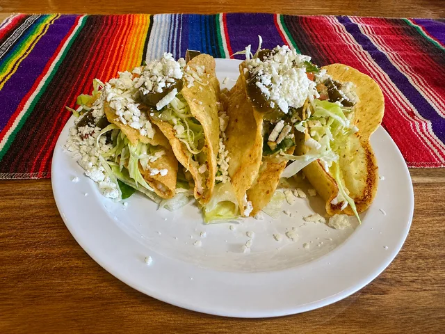 Three crispy tacos topped with lettuce, cheese and jalapeño at Nina's Tacos